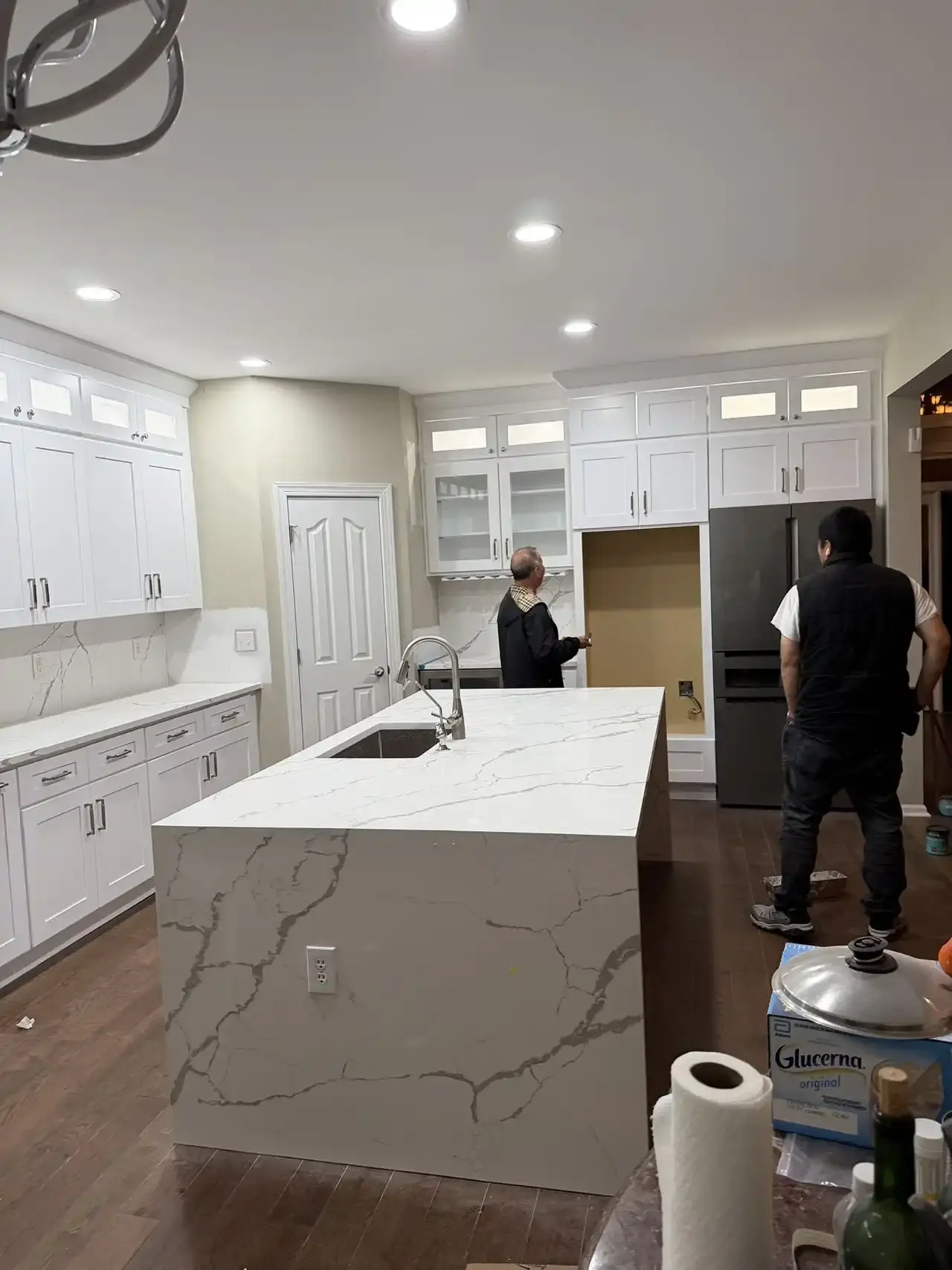 Long kitchen with marble-look waterfall island and glass-front upper cabinets