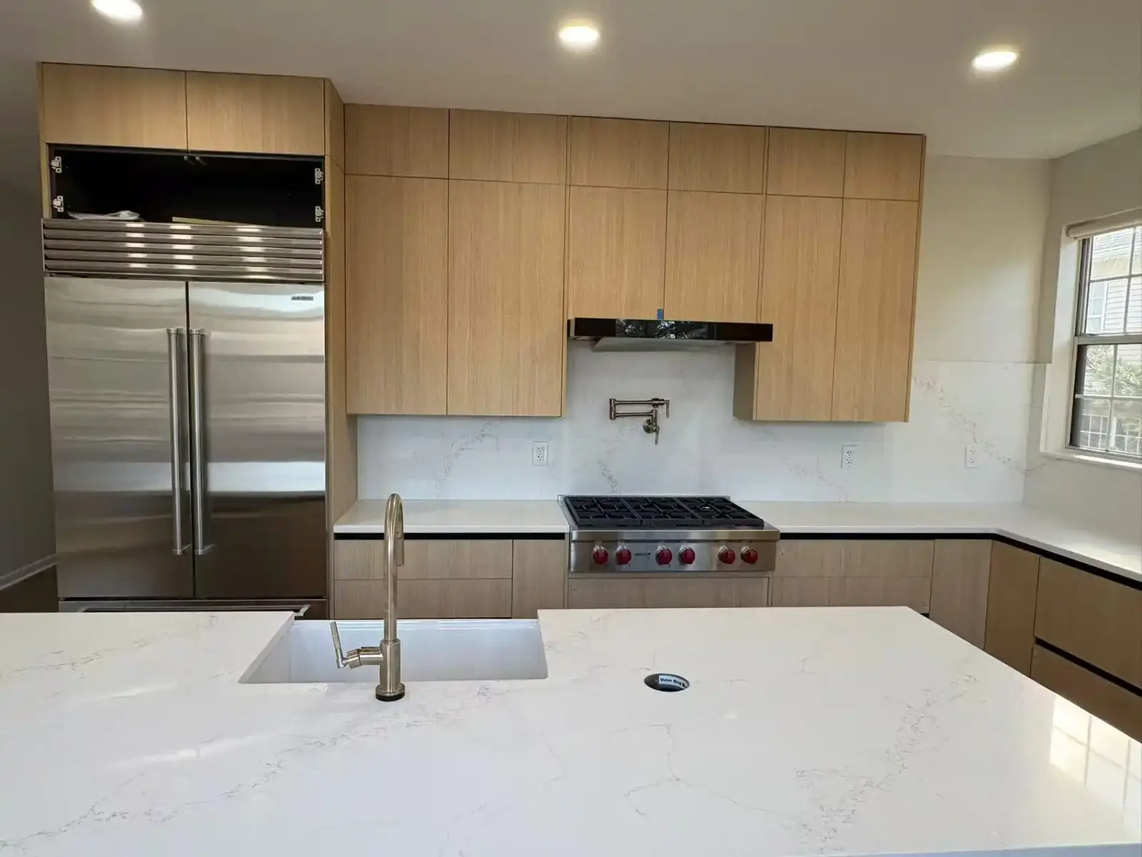 Modern kitchen with light wood cabinetry, professional range and quartz island
